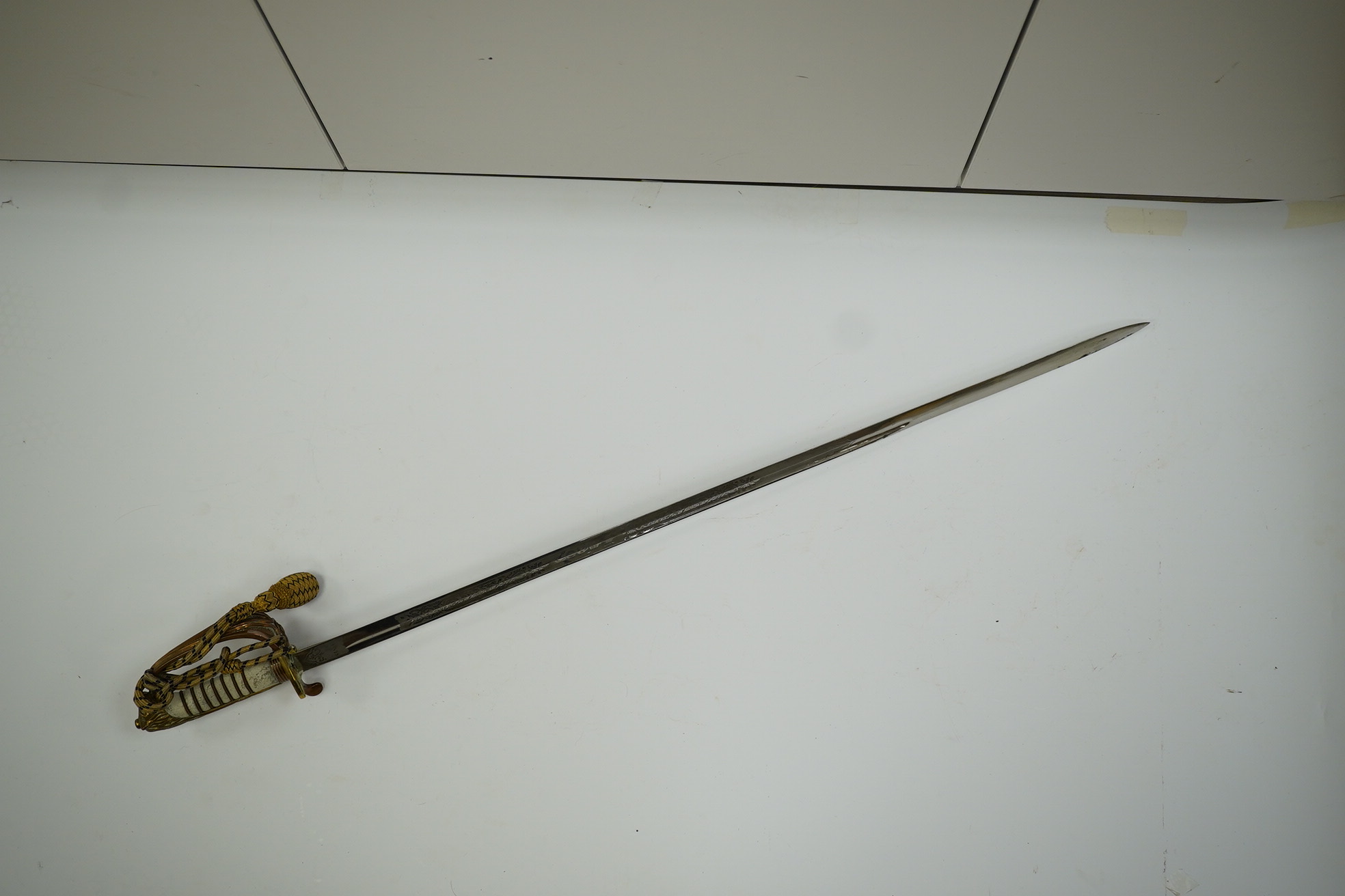 An 1846 pattern naval officer’s sword by Gieves, with folding thumb guard and knot, in its leather scabbard with brass mounts. Together with its outer soft leather cover. Condition - fair, notable wear to grip.